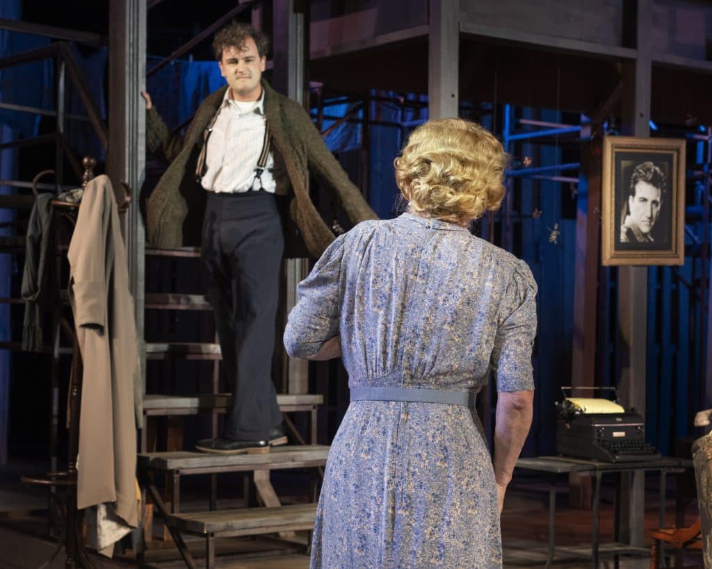 An actor stands on stairs, looking at an actress at the base of the stairs