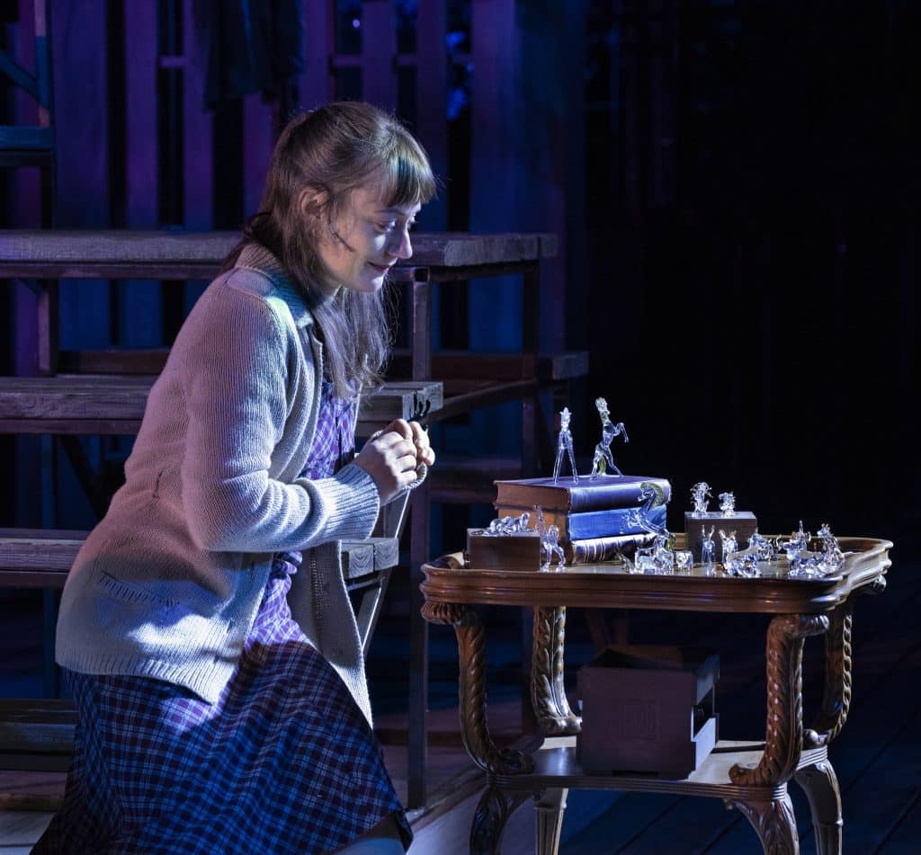 An actress sits, looking at a glass figure collection on a table